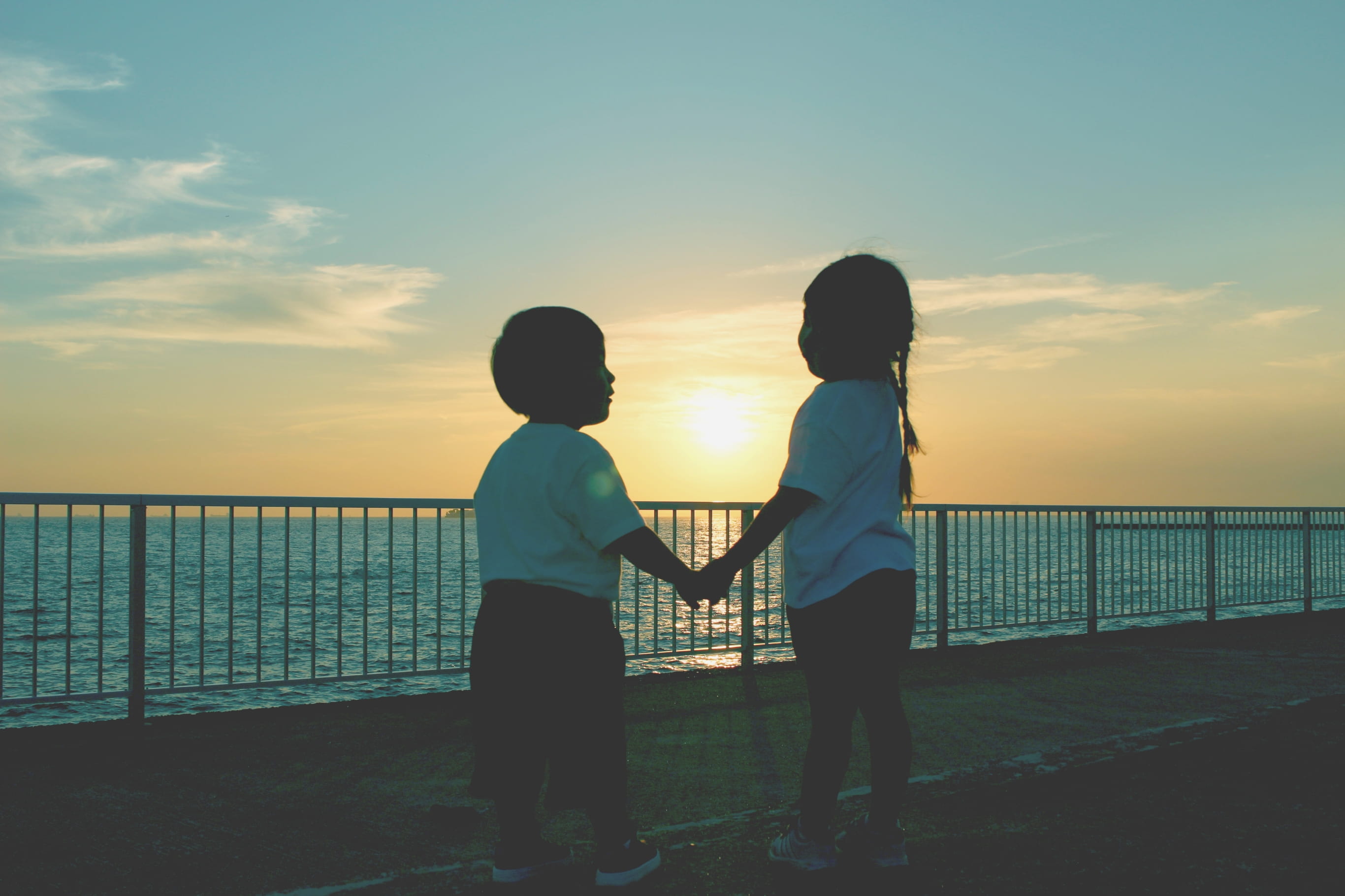 2人の子どもが海と夕日の前で手を繋いでいる様子