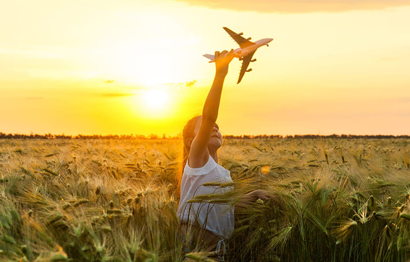 女の子と青空と紙飛行機が飛んでいる様子